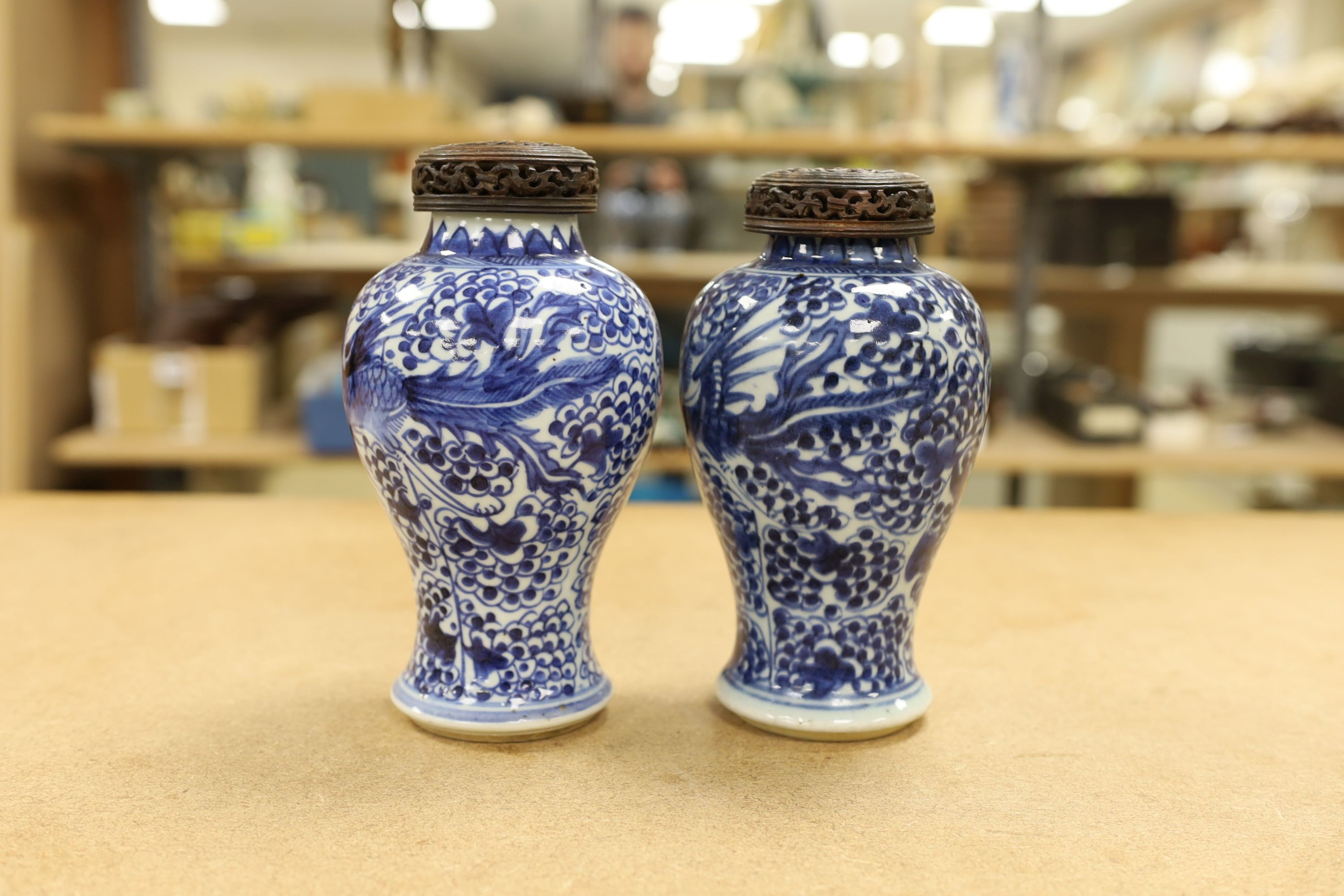 A pair of Chinese blue and white 'phoenix' vases, Kangxi, associated wood covers, 19cm including covers